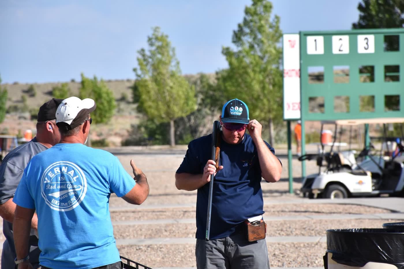 Two club members talking between rounds while another shooter checks his shotgun.