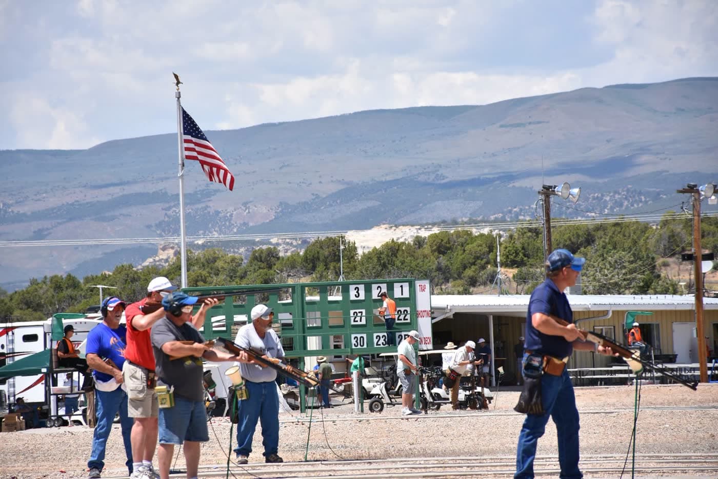 Shooters under the American flag with the squadding scoreboard above the line.